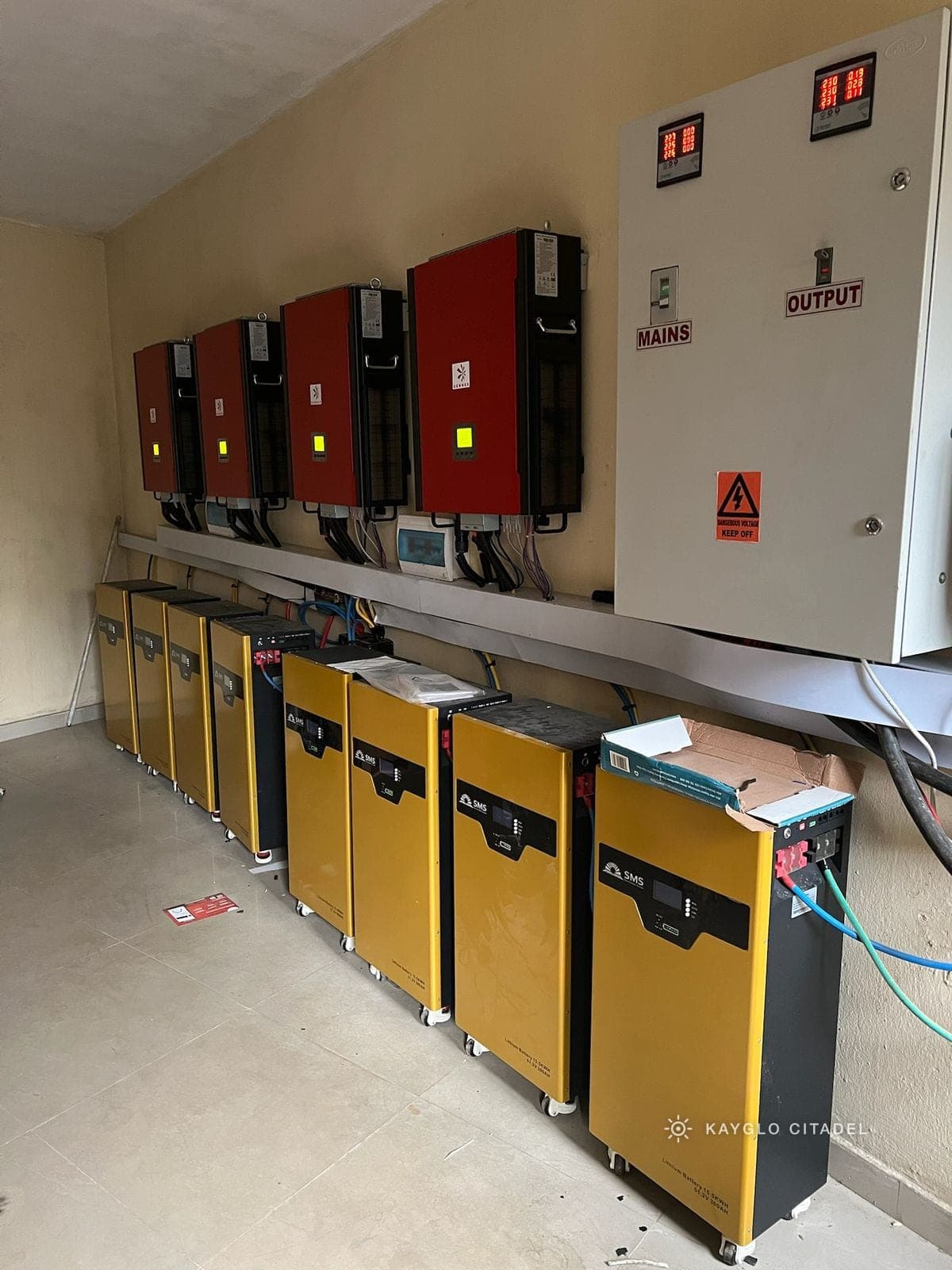 A bank of batteries and four wall-mounted inverters installed in a plant room.