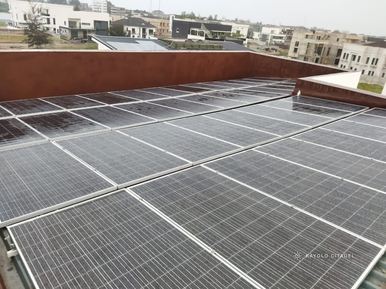 A full rooftop array on a flat estate roof after rain, city skyline behind.
